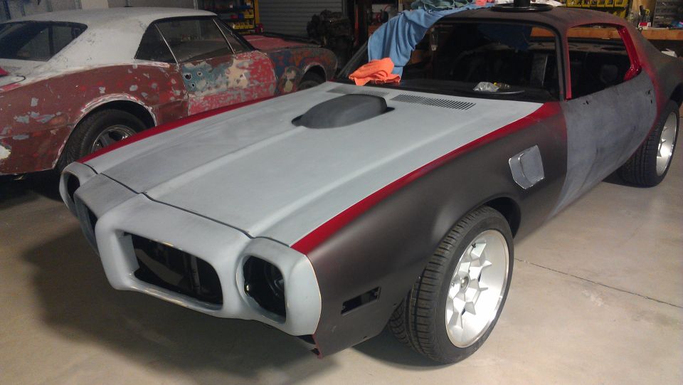 Unfinished 1970s Pontiac Firebird/Trans Am with primer and red stripe detail, seen from a 3/4 front angle