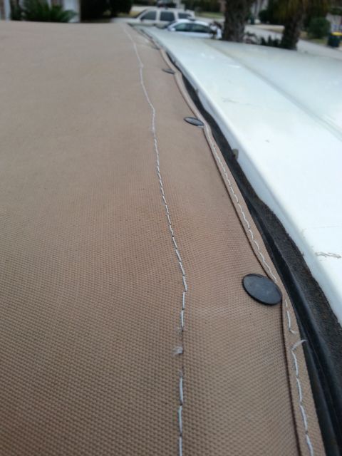 1992 Ford Bronco - Close-up of a tan soft top edge with black snaps and white stitching, showing a bit of the surrounding environment.