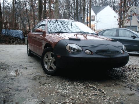 1998 Ford Taurus - A red car with a black hood is parked outdoors, showing its front three-quarter view.