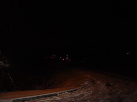 1986 Ford Bronco - A dark, snowy road at night with faint lights in the distance.