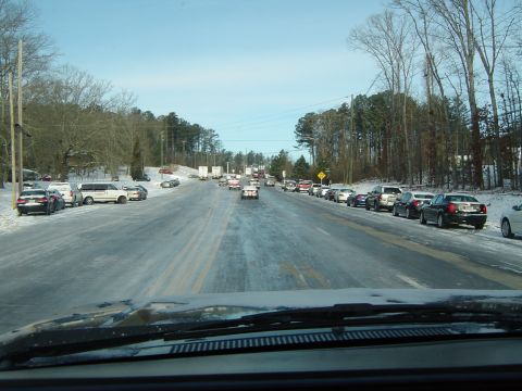 1986 Ford Bronco - Vehicles are stuck in traffic on a slippery, snow-covered road with trees lining the sides.