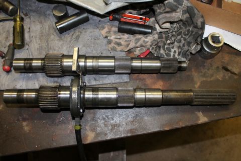 1995 Ford Bronco - Two transfer case shafts are laid out on a workbench, surrounded by tools and rags.