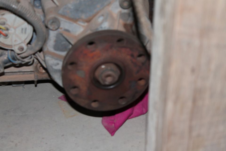 Rusty transfer case flange with bolt holes, attached to a gray metal housing. Pink cloth underneath