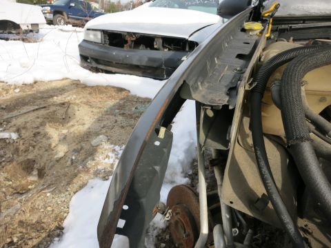 1991 Ford LTD Crown Victoria - Close-up of a damaged car fender and engine bay with snow covering the ground and other vehicles visible.