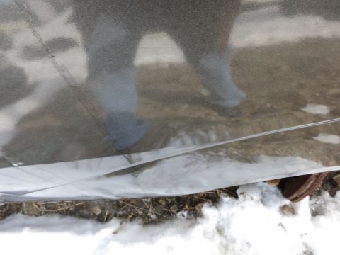 1991 Ford LTD Crown Victoria - Reflection of a person's legs and feet in a shiny, possibly metallic, surface with snow on the ground.