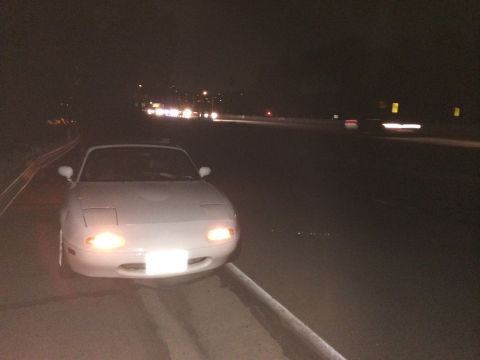 1991 Mazda Miata - 1991 Mazda Miata parked on the side of a highway at night with headlights illuminated.