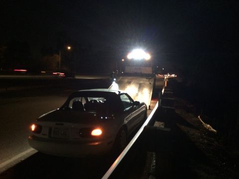 1991 Mazda Miata - A white convertible is loaded onto a tow truck at night, its taillights illuminated on the highway.