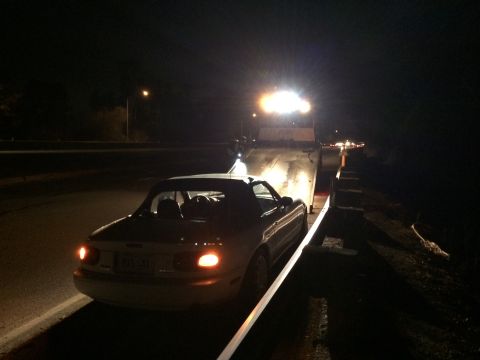1991 Mazda Miata - A white 1991 Mazda Miata is loaded onto a tow truck on a dark road at night.
