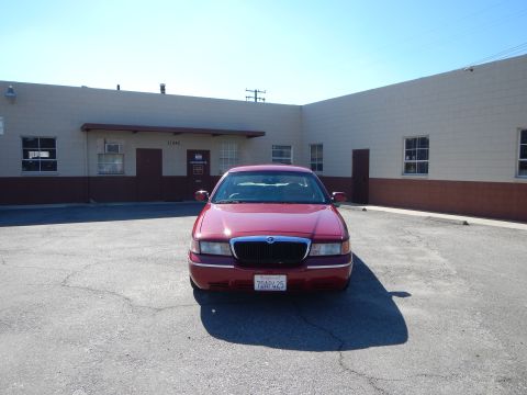 2002 Mercury Grand Marquis - A red 2002 Mercury Grand Marquis is parked in front of a beige and brown building under a clear sky.
