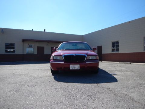 2002 Mercury Grand Marquis - A red 2002 Mercury Grand Marquis is parked in front of a commercial building on a sunny day.