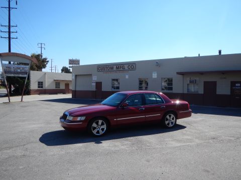 2002 Mercury Grand Marquis - A maroon 2002 Mercury Grand Marquis is parked in a lot in front of a commercial building on a sunny day.