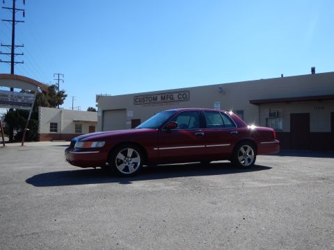 2002 Mercury Grand Marquis - A red 2002 Mercury Grand Marquis sedan is parked in front of a commercial building under a clear blue sky.