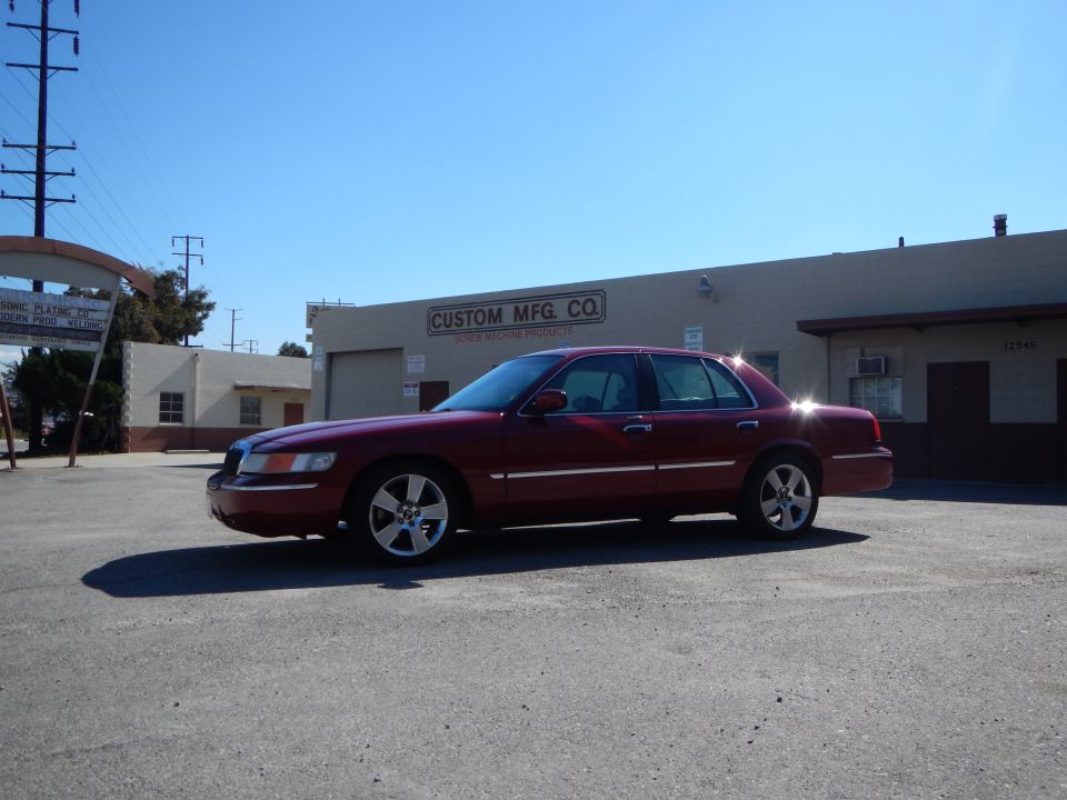 Red 2002 Mercury Grand Marquis sedan parked outside a commercial building, side view