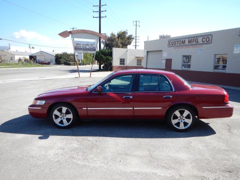 2002 Mercury Grand Marquis - A red 2002 Mercury Grand Marquis sedan is parked on a street in front of a commercial building.