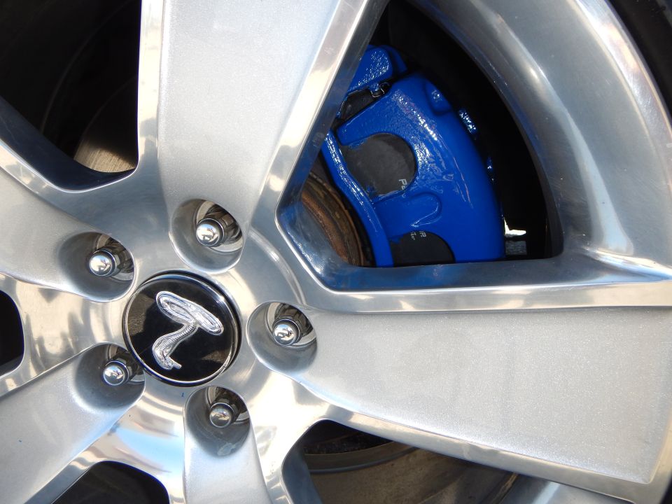 Silver alloy wheel with a blue brake caliper and a black center cap with a silver emblem