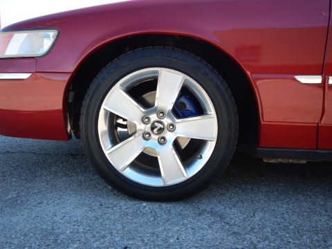2002 Mercury Grand Marquis - The front wheel of a red 2002 Mercury Grand Marquis features silver five-spoke rims and blue brake calipers.