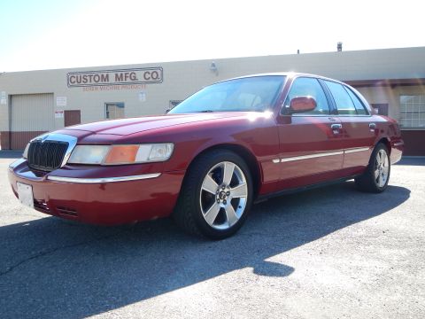 2002 Mercury Grand Marquis - Red 2002 Mercury Grand Marquis with chrome trim and fanblade wheels parked in front of a commercial building.