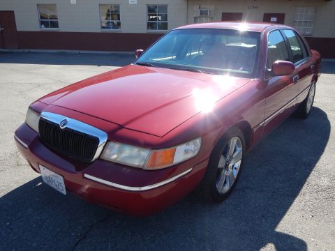 2002 Mercury Grand Marquis - A red 2002 Mercury Grand Marquis is parked in front of a commercial building on a sunny day.