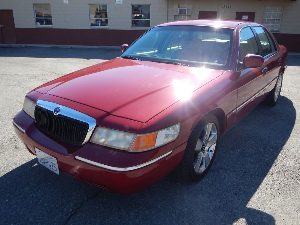 Red 2002 Mercury Grand Marquis parked outside a building. The car has a chrome grille and alloy wheels