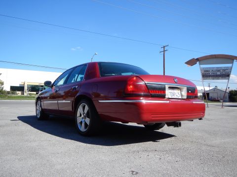 2002 Mercury Grand Marquis - The rear of a red 2002 Mercury Grand Marquis is shown parked in a lot with a sign in the background.