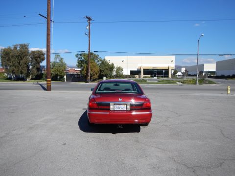 2002 Mercury Grand Marquis - The rear of a red 2002 Mercury Grand Marquis is visible in a parking lot under a clear blue sky.