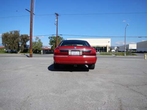 2002 Mercury Grand Marquis - The rear of a red 2002 Mercury Grand Marquis sedan is visible in a parking lot under a clear blue sky.