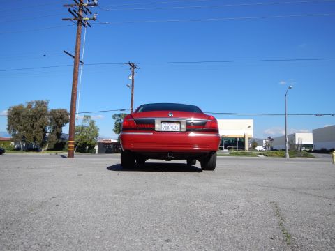 2002 Mercury Grand Marquis - Rear view of a red 2002 Mercury Grand Marquis parked in a lot under a clear blue sky.