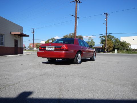 2002 Mercury Grand Marquis - Rear view of a red 2002 Mercury Grand Marquis parked in an asphalt lot under a clear blue sky.