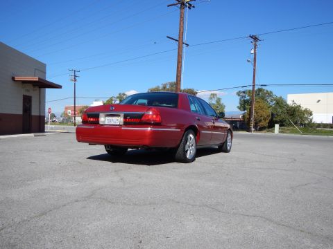 2002 Mercury Grand Marquis - The rear of a red 2002 Mercury Grand Marquis is shown parked in an asphalt lot under a clear blue sky.