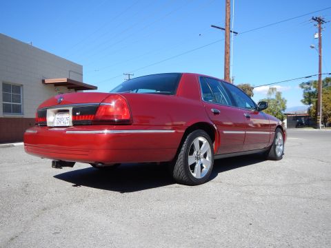 2002 Mercury Grand Marquis - A red 2002 Mercury Grand Marquis sedan is shown from the rear three-quarter angle, chrome accents and distinctive aftermarket wheels.