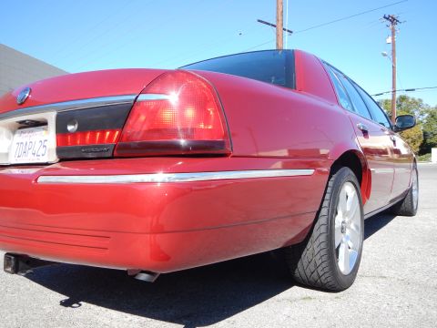 2002 Mercury Grand Marquis - The rear of a red 2002 Mercury Grand Marquis is shown from a low angle, highlighting its taillight and chrome accents.
