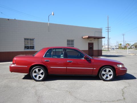 2002 Mercury Grand Marquis - Side profile of a red 2002 Mercury Grand Marquis with aftermarket wheels parked outdoors.