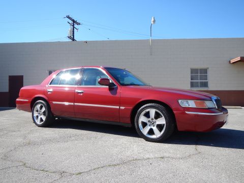 2002 Mercury Grand Marquis - This red 2002 Mercury Grand Marquis sedan is shown from a three-quarter front angle, highlighting its chrome accents and distinctive wheels.