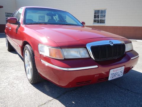 2002 Mercury Grand Marquis - A red sedan is parked outside a building on a sunny day. The vehicle has a chrome grille and a California license plate.