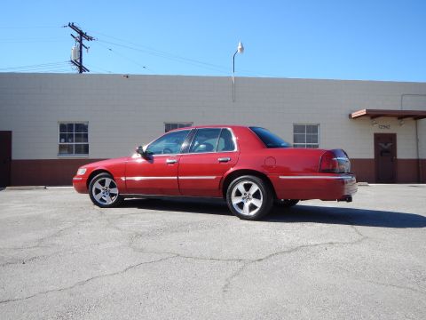 2002 Mercury Grand Marquis - A red 2002 Mercury Grand Marquis sedan is parked in a lot, viewed from the side. The vehicle features aftermarket wheels.