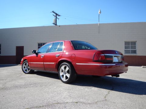 2002 Mercury Grand Marquis - A red sedan is parked on asphalt in front of a light-colored building under a clear blue sky.