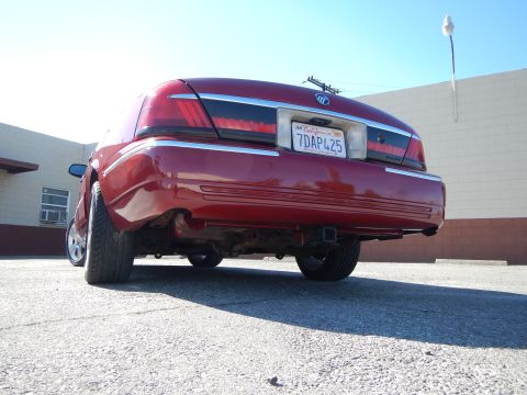 2002 Mercury Grand Marquis - The rear of a red sedan is shown, a trailer hitch and a California license plate.