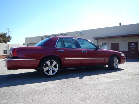 2002 Mercury Grand Marquis - Side profile of a red 2002 Mercury Grand Marquis with custom wheels parked outdoors.