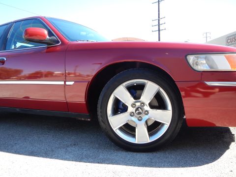 2002 Mercury Grand Marquis - This red sedan, likely a 2003 model, is shown from the front passenger side, highlighting its chrome wheels and blue brake calipers.