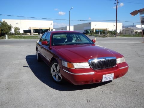 2002 Mercury Grand Marquis - Red 2002 Mercury Grand Marquis parked on asphalt with commercial buildings in the background.