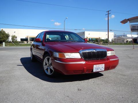 2002 Mercury Grand Marquis - A red 2002 Mercury Grand Marquis is parked on asphalt under a clear blue sky.