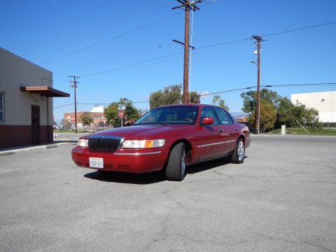 2002 Mercury Grand Marquis - A red 2002 Mercury Grand Marquis sedan is parked in a lot under a clear blue sky.