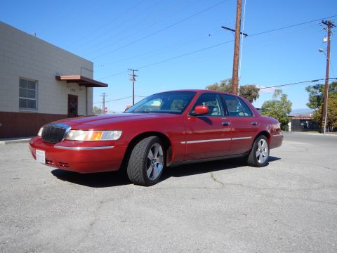 2002 Mercury Grand Marquis - A red 2002 Mercury Grand Marquis sedan is parked on a street under a clear blue sky.