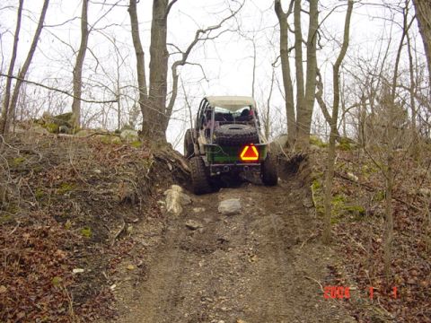1992 Ford Bronco - A modified off-road vehicle navigates a challenging, muddy, and rocky incline through a wooded area.