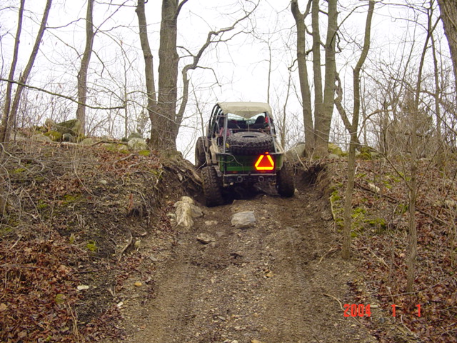 off-road vehicle with spare tire on back climbing a rocky, wooded trail