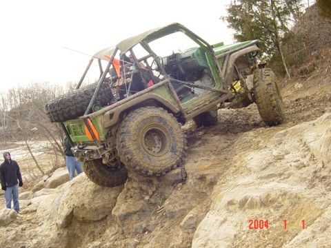 1992 Ford Bronco - Modified off-road vehicle navigates a rocky, muddy incline with a spare tire mounted on the back.