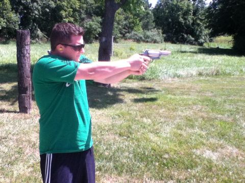 2006 Ford E350 - A man practices shooting a handgun in a grassy outdoor area.