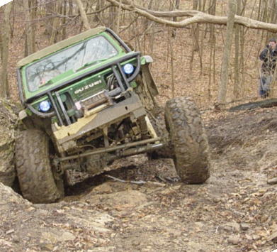 1992 Ford Bronco - A green Suzuki navigates a challenging off-road course in a wooded area.