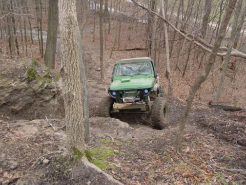 1992 Ford Bronco - A green off-road vehicle navigates a challenging, wooded terrain.