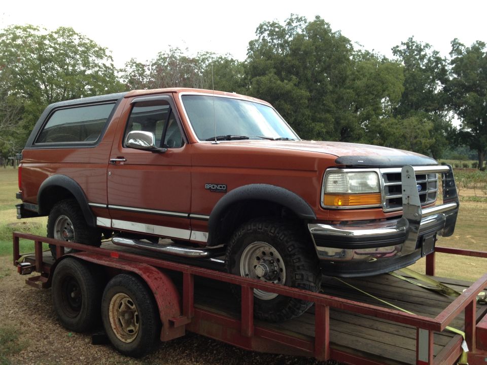 Orange Ford Bronco on a trailer, front 3/4 view. Chrome bumper and side trim visible